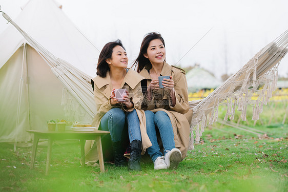 坐在吊床上的姐妹拿着水杯图片