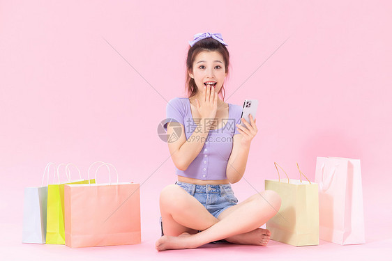 坐在购物袋旁的美女看着手机惊喜图片