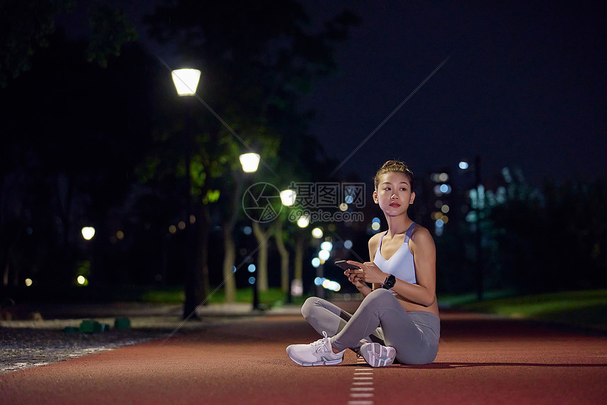 夜晚在公园健身的人坐在跑道上休息图片