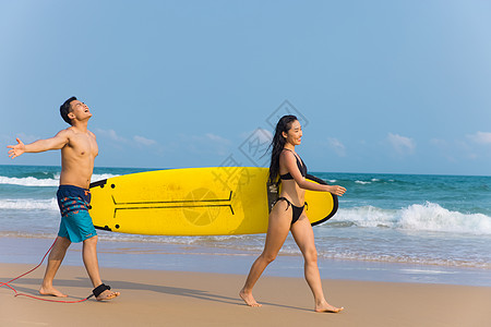 大海美女青年情侣拿着冲浪板海边沙滩上行走背景