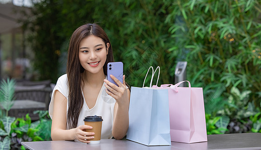 美女购物消费坐在室外咖啡厅看手机图片