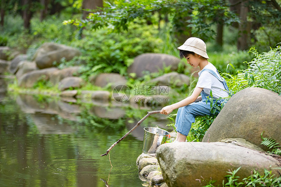 在户外小溪边钓鱼的小男孩图片