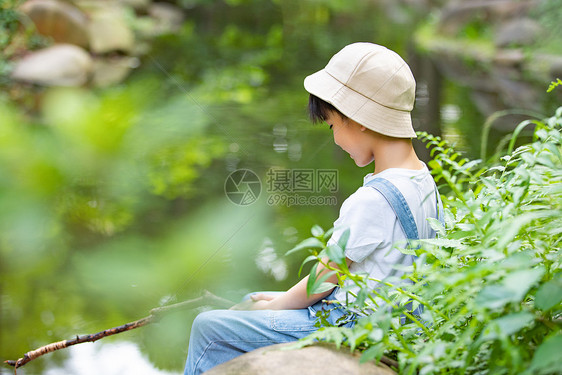 在户外小溪边专注钓鱼的小男孩图片