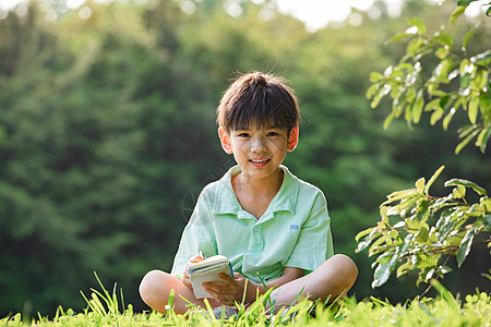 坐在草地上写观察日记的小男孩图片