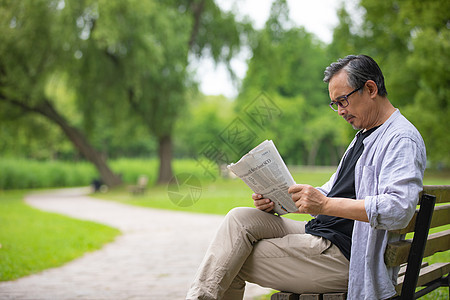 中年男性坐在公园椅子上看报纸图片