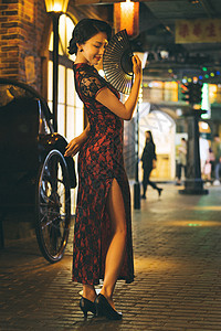 城市夜晚霓虹灯下扇子遮面的旗袍美女图片