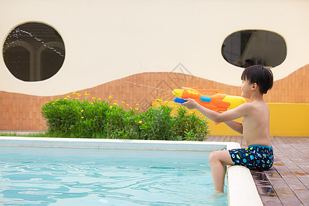 小男孩坐在泳池边玩水枪玩具图片