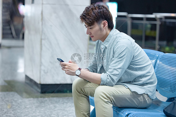年轻男性坐在地铁站看手机图片