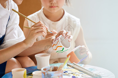 艺术老师教小朋友陶罐作画特写图片