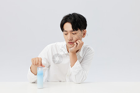 韩系帅哥低头看手上拿的乳液瓶图片