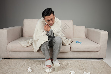 中年男子患感冒坐在沙发上用毯子保暖背景图片
