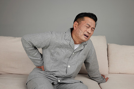 孤独坐在山上中年男子坐在沙发上扶着腰面带痛苦背景