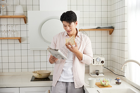 帅气的年轻男士在厨房吃早餐读报纸图片