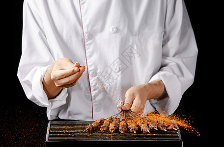 厨师正在给羊肉串撒辣椒粉背景图片