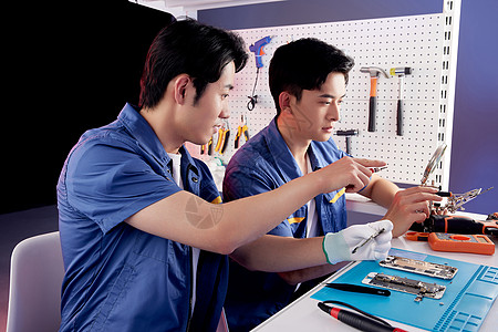 工人合作前辈在指导年轻的维修工修理电脑背景
