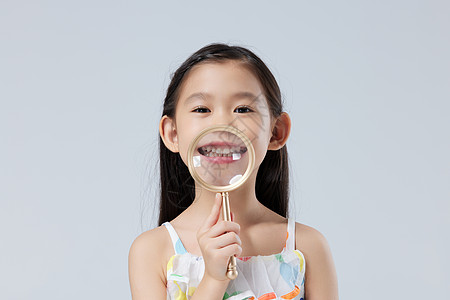 可爱小女孩拿放大镜检查牙齿背景图片