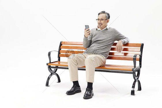 老年人坐在长椅上玩手机图片