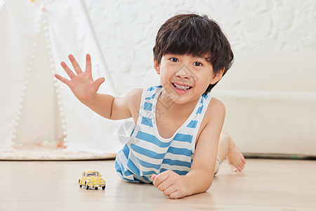 小男孩趴在地板上玩玩具车背景图片