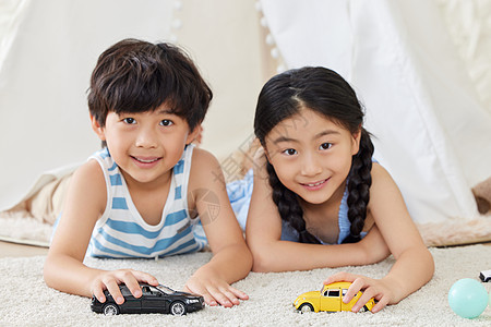 两个小朋友趴在地毯上玩汽车模型图片