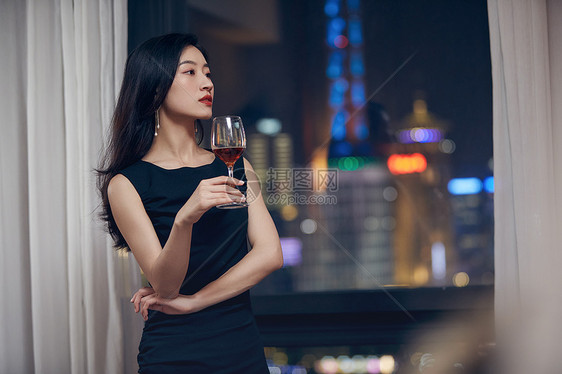 气质美女夜晚端着红酒杯站在窗前图片