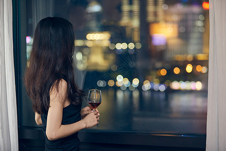 美女夜晚端着红酒杯站在窗前背影高清图片