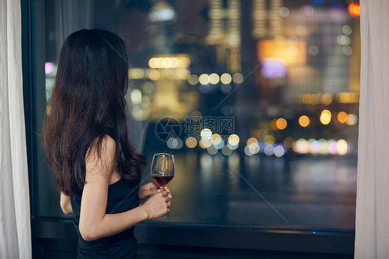美女夜晚端着红酒杯站在窗前背影图片