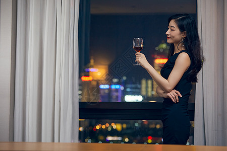 气质美女夜晚端着红酒杯站在窗前背景图片
