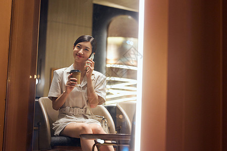 商务女青年喝水夜晚在咖啡店打电话的商务女性背景