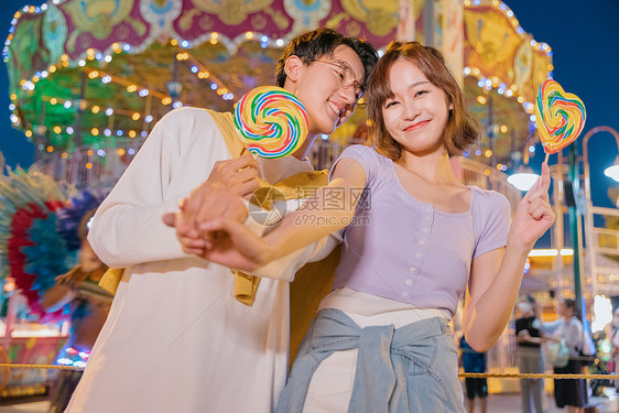 甜蜜的情侣拿着棒棒糖在游乐场玩耍图片