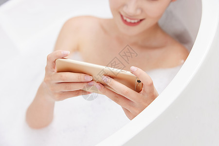 年轻女性洗泡泡浴玩手机特写图片