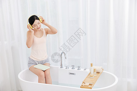 年轻女性坐在浴缸前看书听音乐图片