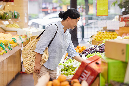 蔬菜市场中年女性水果店内挑选水果背景