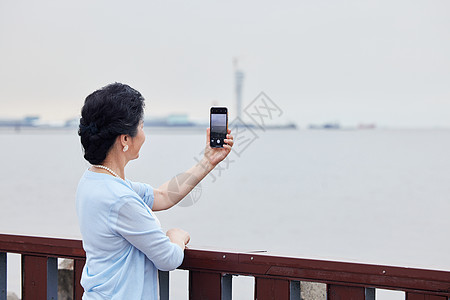 重阳字奶奶拿着手机对海边拍风景背景