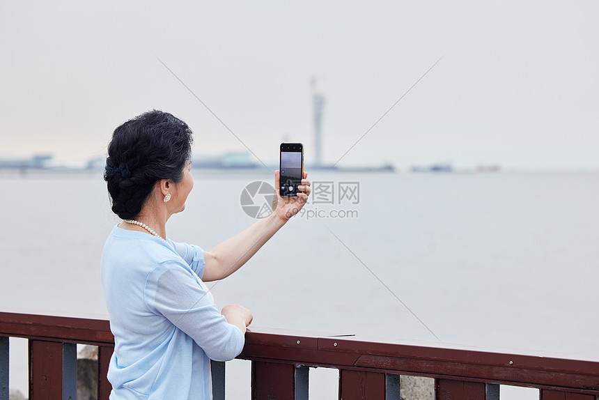 奶奶拿着手机对海边拍风景图片