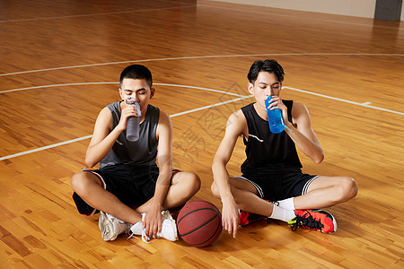 两个篮球运动青年坐在室内篮球场地板上休息图片