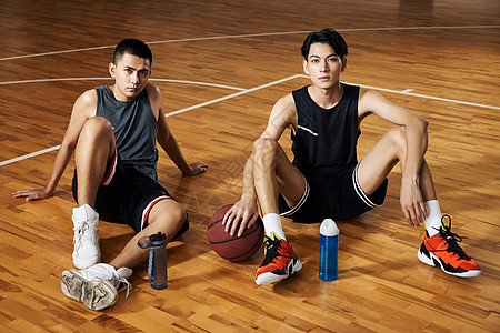 运动饮料两个篮球运动青年坐在室内篮球场休息背景