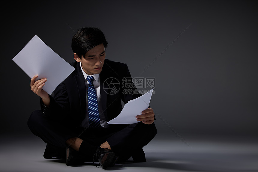 手拿文件坐在地上的男性图片
