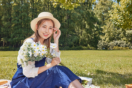 青春活跃美女户外草坪上手捧鲜花野餐郊游背景