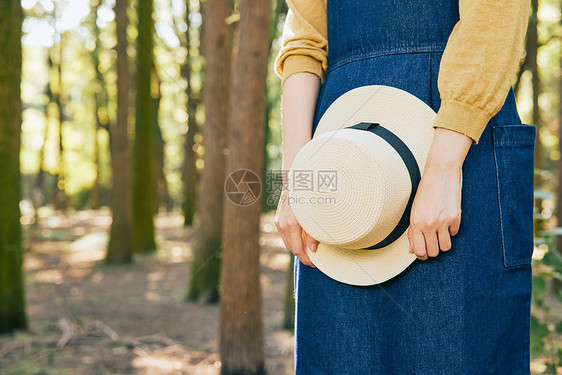 女性手拿草帽在森林里背影特写图片