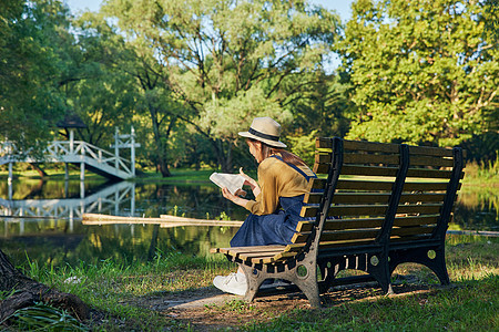 美女公园湖边长椅上看书阅读背影背景图片