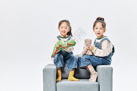 可爱调皮双胞胎小女孩沙发上玩绒毛玩偶图片