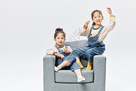 儿童双胞胎小女孩坐沙发上玩小鸭子玩具背景图片