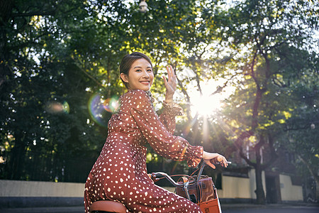 骑自行的女孩清新美女坐在自行车上回头打招呼背景