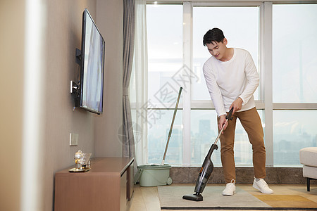 年轻男性居家使用吸尘器清洁地毯图片