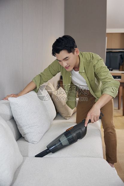 男青年使用吸尘器清洁沙发图片