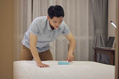 年轻男士使用粘毛器滚刷床单图片