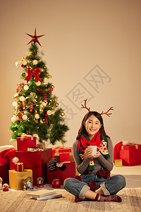 圣诞节美女手拿杯子坐在圣诞树和礼物前图片