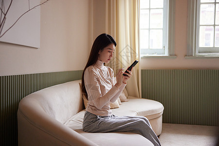 年轻美女坐在沙发上玩手机图片