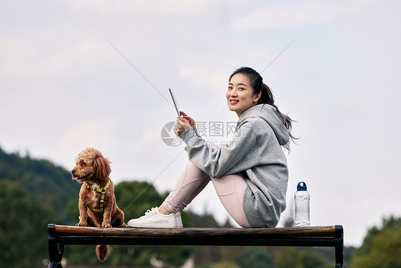 坐在长椅上看平板的运动少女和萌宠泰迪图片