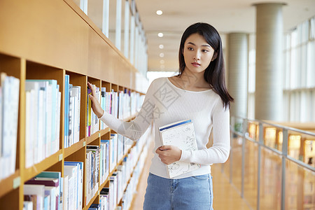 女学生在图书馆书架前挑选书籍高清图片